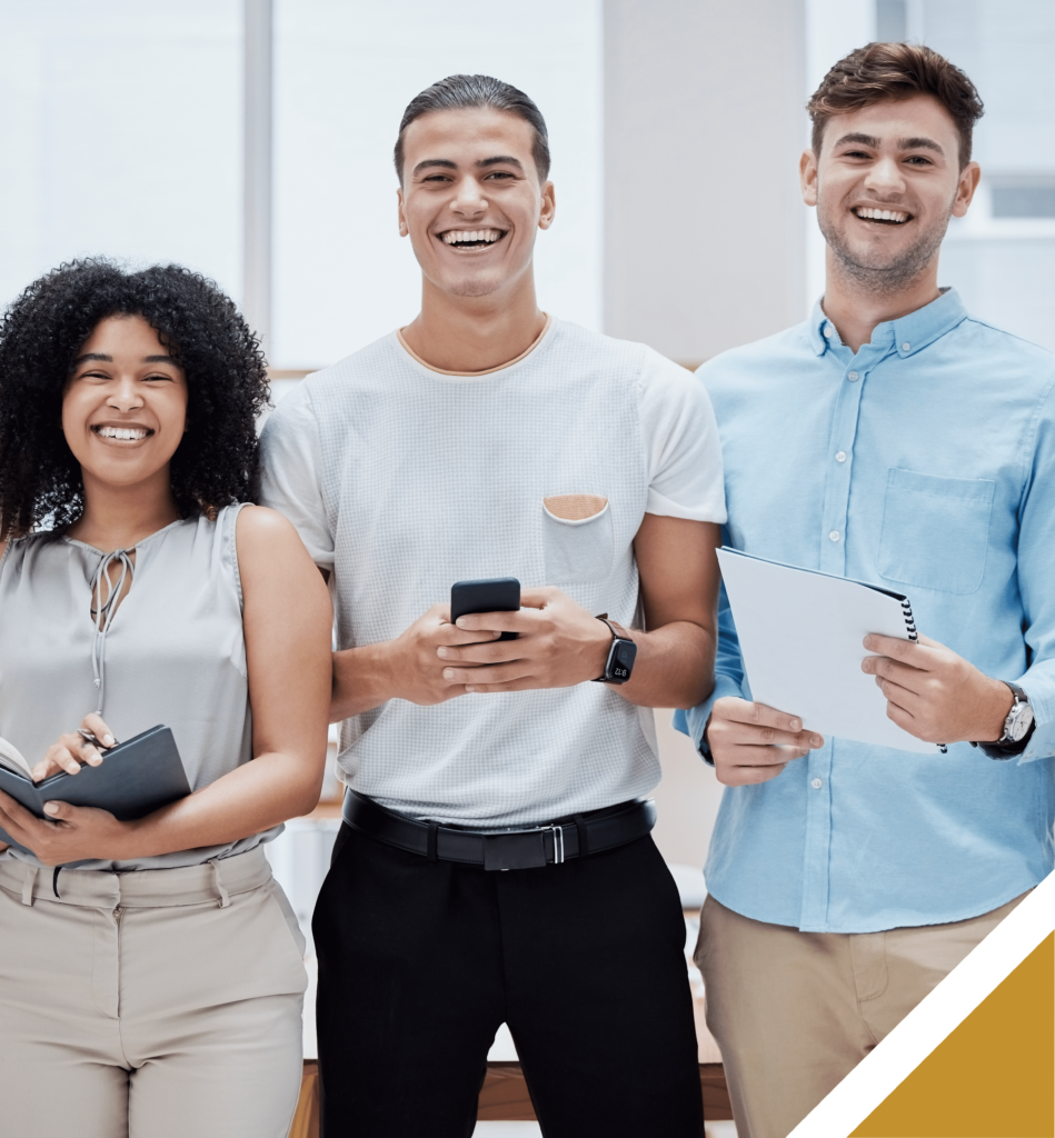Kaksi miestä ja yksi nainen eri kulttuureista hymyilevät ja pitävät kädessä mobiililaitteita. Kuva otettu ulkomaisessa työympäristössä.